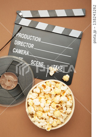 Movie clapper with popcorn and film reels on brown background Movie clapper with popcorn and film reels on brown background 138243262