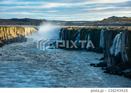 The waterfall in Selfoss, Iceland showcases powerful flowing water amidst dramatic cliffs and a vast natural landscape. Sunlight reflects off the water, creating an inviting scene for nature lovers. The waterfall in Selfoss, Iceland showcases powerful flowing water amidst dramatic cliffs and a vast natural landscape. Sunlight reflects off the water, creating an inviting scene for nature lovers. 138243428
