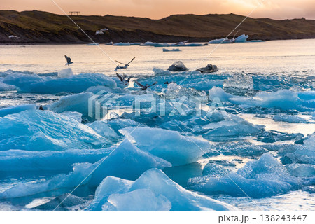 Icebergs float in Iceland's glacier lagoon, reflecting the warm colors of sunset. Birds fly above, adding life to the tranquil scene. This location is a must-see for nature enthusiasts. Icebergs float in Iceland's glacier lagoon, reflecting the warm colors of sunset. Birds fly above, adding life to the tranquil scene. This location is a must-see for nature enthusiasts. 138243447