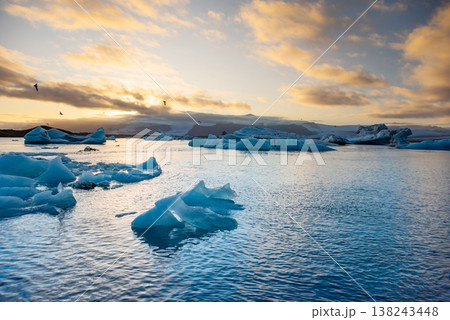 Icebergs float in Iceland's glacier lagoon, reflecting the warm colors of sunset. Birds fly above, adding life to the tranquil scene. This location is a must-see for nature enthusiasts. Icebergs float in Iceland's glacier lagoon, reflecting the warm colors of sunset. Birds fly above, adding life to the tranquil scene. This location is a must-see for nature enthusiasts. 138243448