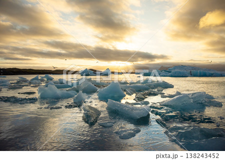 Icebergs float in Iceland's glacier lagoon, reflecting the warm colors of sunset. Birds fly above, adding life to the tranquil scene. This location is a must-see for nature enthusiasts. Icebergs float in Iceland's glacier lagoon, reflecting the warm colors of sunset. Birds fly above, adding life to the tranquil scene. This location is a must-see for nature enthusiasts. 138243452