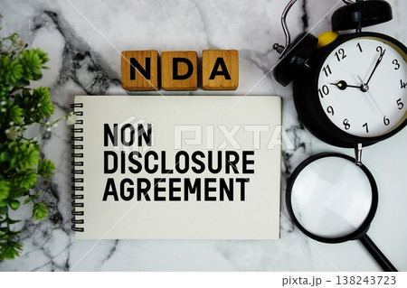 NDA Non Disclosure Agreement text with alarm clock and magnifying glass on marble background NDA Non Disclosure Agreement text with alarm clock and magnifying glass on marble background 138243723
