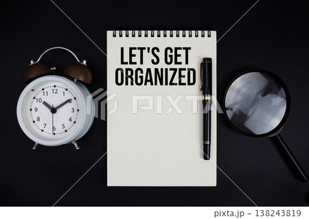 Let's Get Organized text written on notepad with alarm clock top view on black background Let's Get Organized text written on notepad with alarm clock top view on black background 138243819