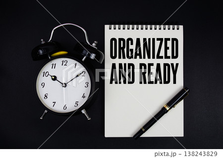 Organized And Ready text written on notepad with alarm clock top view on black background 138243829