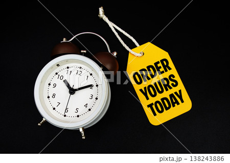 Price tag with message "Order Yours Today" and alarm clock on black background Price tag with message "Order Yours Today" and alarm clock on black background 138243886