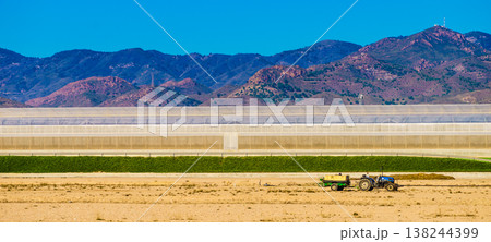 Tractor working near large greenhouse with mountains in background. Region of Mazarron, Sierra de las Moreras in Murcia Spain. Tractor working near large greenhouse with mountains in background. Region of Mazarron, Sierra de las Moreras in Murcia Spain. 138244399