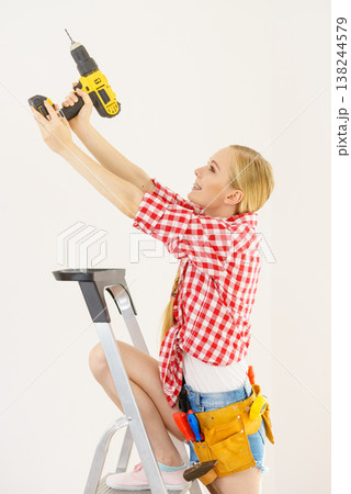 Woman on ladder using drill 138244579