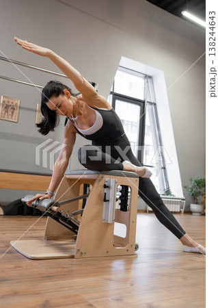 Woman doing side plank pilates variation on wooden box in sleek fitness studio. Side plank, pilates, wooden box, studio, workout. Woman doing side plank pilates variation on wooden box in sleek fitness studio. Side plank, pilates, wooden box, studio, workout. 138244643