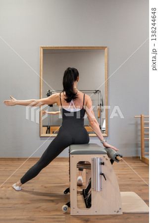 Woman stretching side body on wooden pilates box wearing black sportswear in bright studio. Side stretch, pilates box, studio, black sportswear, fitness. 138244648