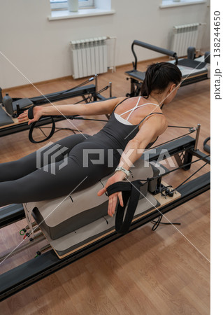 Athletic woman in leggings working pilates reformer and exercising legs in sunlit fitness studio. Pilates reformer, legs, exercising, studio, athletic. Athletic woman in leggings working pilates reformer and exercising legs in sunlit fitness studio. Pilates reformer, legs, exercising, studio, athletic. 138244650