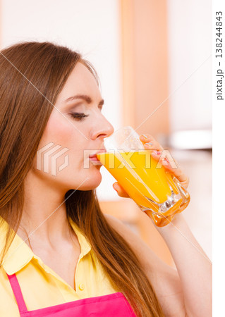 Woman in kitchen drinking fresh orange juice 138244843