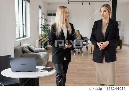 Businesswomen engaging in a conversation, collaborating and communicating in a contemporary open plan office setting, fostering teamwork and professional interaction Businesswomen engaging in a conversation, collaborating and communicating in a contemporary open plan office setting, fostering teamwork and professional interaction 138244913