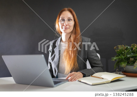 Woman working on laptop while smiling at camera 138245288