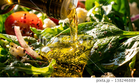 Pouring golden olive oil onto a fresh green salad with tomatoes and feta cheese 138246889