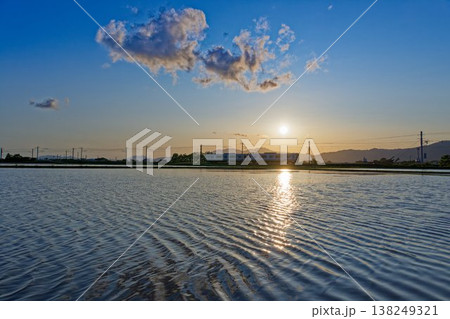 水田一面に水を張った夕映えの佐賀平野を行くJR長崎本線の普通列車 138249321