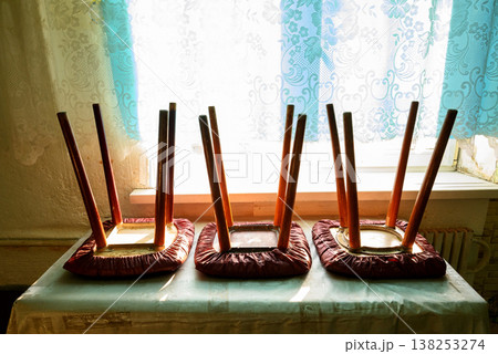 three upturned stools stand on a table in front of a window with curtains on a sunny day three upturned stools stand on a table in front of a window with curtains on a sunny day 138253274