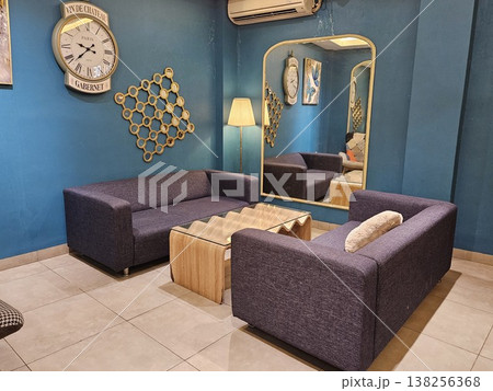 A stylish modern living room interior featuring purple fabric sofas, a unique wavy wooden coffee table, and a large vintage wall clock against deep teal walls with a tall arched gold-framed mirror. 138256368