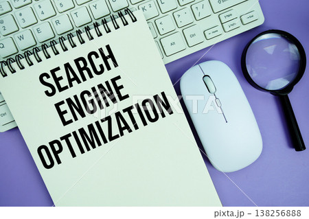 Notepad with the text "Search Engine Optimization" and white keyboard, wireless mouse, magnifying glass and alarm clock 138256888