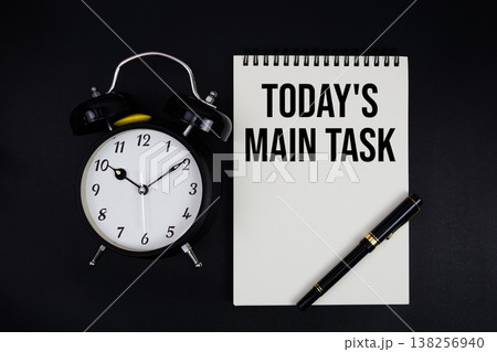 Today's Main Task text written on notepad with alarm clock top view on black background Today's Main Task text written on notepad with alarm clock top view on black background 138256940