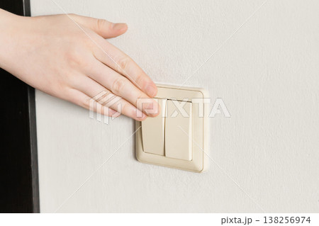 Hand pressing beige light switch on white wall, turning on or off power Hand pressing beige light switch on white wall, turning on or off power 138256974