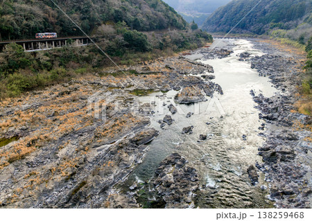 川面が夕日に照らされて輝く四万十川に架かる半家沈下橋を遠望していたら予土線の気動車がやって来た 138259468