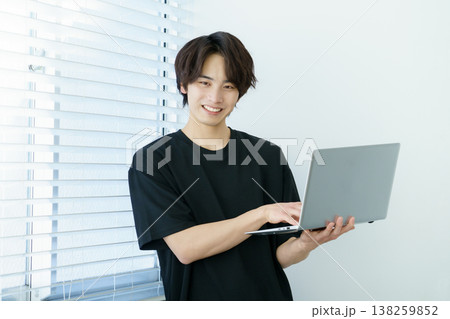 窓際に立ってノートパソコンを操作する若い日本人男性のポートレート 窓際に立ってノートパソコンを操作する若い日本人男性のポートレート 138259852