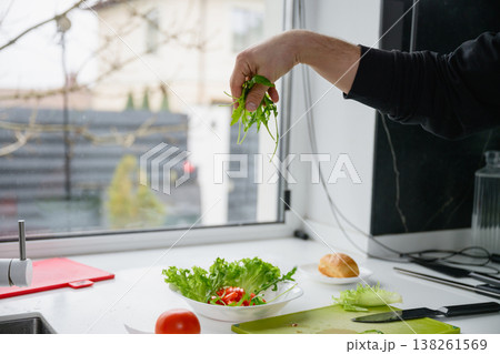 Male hand sprinkling fresh green arugula over a healthy vegetable salad in a white bowl 138261569