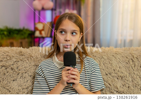 Child girl kid shyly sings alone into microphone sitting on sofa, smiling quietly with joy at home 138261916