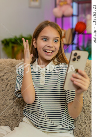 Child girl kid playing mobile game app on smartphone at home, smiling and celebrating happy victory Child girl kid playing mobile game app on smartphone at home, smiling and celebrating happy victory 138262323