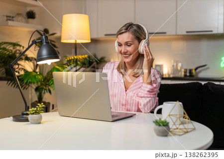 Adult woman in headphones tweaks layout on laptop moves layers nods to music smiles saves version 138262395