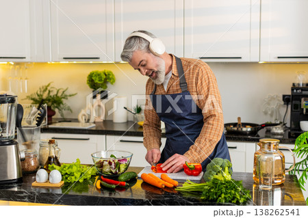 Middle-aged man chopping red pepper wearing headphones enjoying music while preparing healthy meal Middle-aged man chopping red pepper wearing headphones enjoying music while preparing healthy meal 138262541