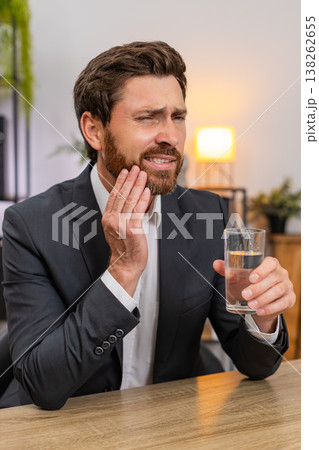 Middle-aged businessman drinks cold water winces tooth pain urgently searches dentist via smartphone 138262655
