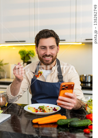 Middle-aged man enjoying fresh salad meal in kitchen checking smartphone for health diet success app Middle-aged man enjoying fresh salad meal in kitchen checking smartphone for health diet success app 138262749