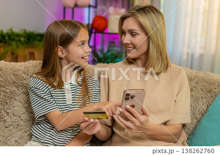 Child girl kid shopping online with mother using smartphone and credit card sitting on home sofa Child girl kid shopping online with mother using smartphone and credit card sitting on home sofa 138262760