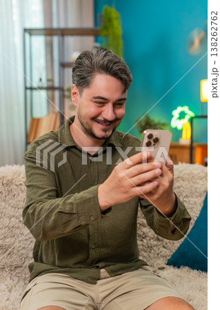 Middle-aged man happy smiling nodding reading smartphone message relaxing on home sofa couch indoors 138262762