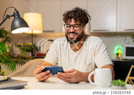 Arabian man in headphones laughs at podcast on smartphone leaves like and writes review in app late 138263148