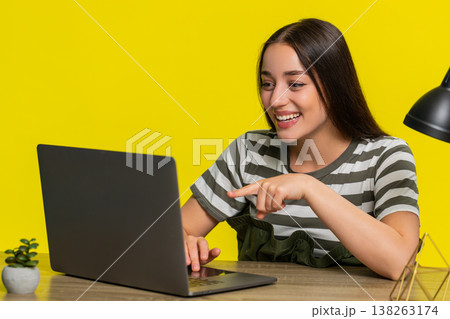 Woman at table laughing while scrolling laptop screen watching funny entertaining online content 138263174