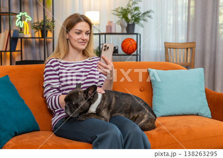 Middle-aged woman with dog scrolls social media on smartphone pet in arms calm mood simple lifestyle 138263295