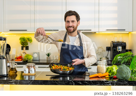 Middle-aged man tasting vegetables on skillet pan at home kitchen cooking healthy diet meal on stove 138263296