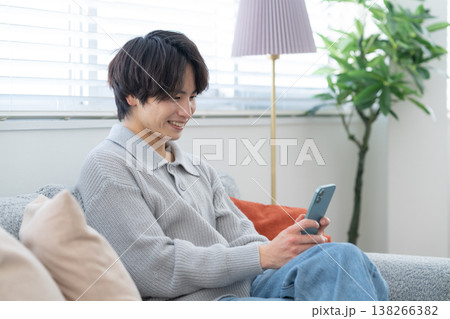 リビングの窓際でスマホを見る若い男性 リビングの窓際でスマホを見る若い男性 138266382