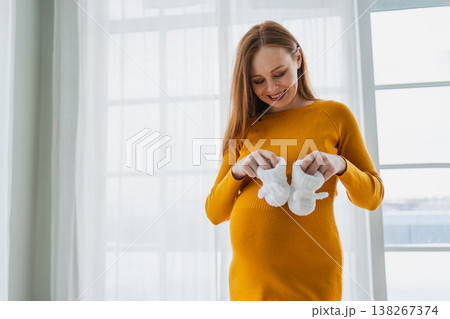 Pregnancy motherhood people expectation future. Pregnant woman with big belly holding newborn baby booties smiling at home. Young mom enjoying pregnancy. Maternity tenderness parenthood new life 138267374