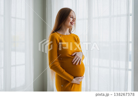 Pregnancy motherhood people expectation future. Pregnant woman with big belly standing near window at home. Girl hugging her tummy enjoying pregnancy. Maternity tenderness parenthood new life concept 138267378