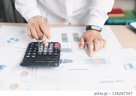 Business analyst calculating figures on calculator and pointing at summary report charts, reviewing financial data for budgeting, accounting, audit, taxation, KPI tracking and forecasting decisions. 138267387