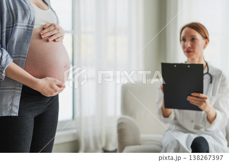 Pregnant woman hands touching big belly in doctor office. Female doctor examining pregnant woman. Gynecologist doctor consulting patient about pregnancy in hospital. Visit to doctor medical checkup 138267397