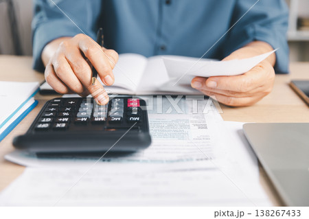 Close-up hands calculating taxes with calculator and pen, holding receipt over tax form on office desk, showing income filing, compliance, deductions, refunds and audit preparation. tax, compliance 138267433
