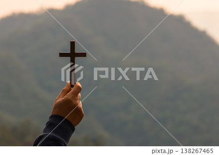 Hand holding wooden cross in front of misty mountain at sunrise, symbol of Christian faith, prayer, worship and hope. Spiritual background with copy space for inspirational design. spiritual Christian Hand holding wooden cross in front of misty mountain at sunrise, symbol of Christian faith, prayer, worship and hope. Spiritual background with copy space for inspirational design. spiritual Christian 138267465