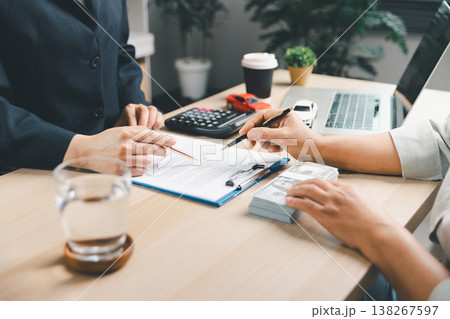 Close-up of client and agent signing car loan contract at office desk with cash, calculator, laptop and model cars, symbolizing auto finance, insurance, payment approval, business trust. agent signing 138267597