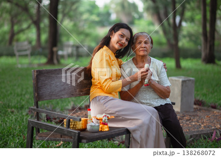 Young woman sitting beside an elderly woman with a jasmine garland after a Songkran blessing, portraying Thai family bonding, respect for elders, affection and authentic cultural tradition. 138268072