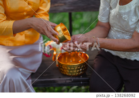 Close up of a traditional Thai water blessing with a golden bowl and gentle hands, illustrating Songkran respect for elders, gratitude, family care and meaningful cultural heritage. Close up of a traditional Thai water blessing with a golden bowl and gentle hands, illustrating Songkran respect for elders, gratitude, family care and meaningful cultural heritage. 138268092