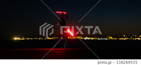 Woman wielding powerful red light blades in dark cityscape Woman wielding powerful red light blades in dark cityscape 138269535